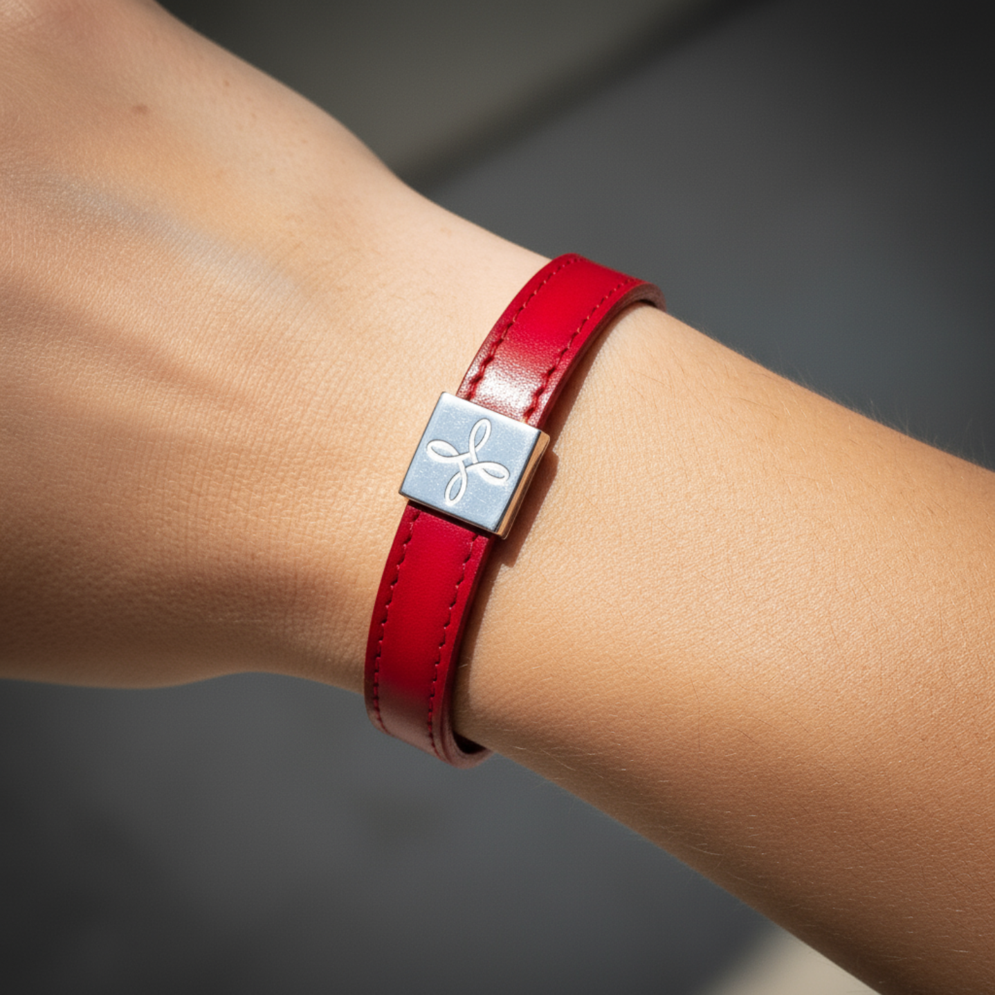 Red leather bracelet with a silver clasp on a wrist against a gray background