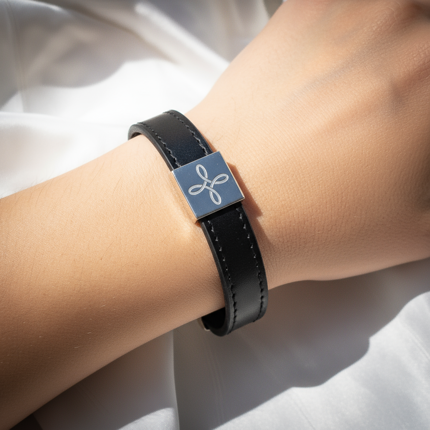 Black leather bracelet with a silver square clasp on a wrist against a white background