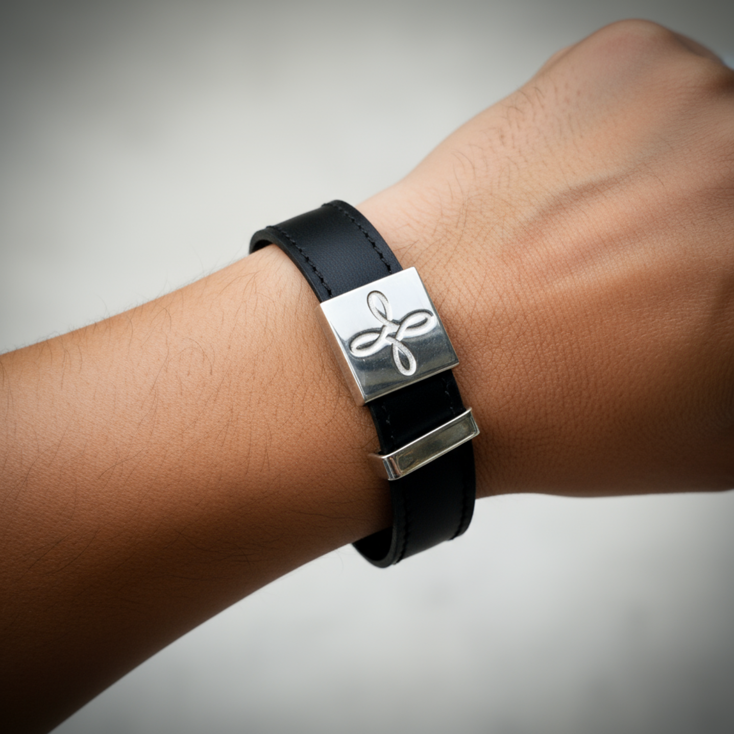 Black leather bracelet with a silver clasp on a wrist against a gray background